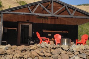 A rustic cabin with a wooden exterior, a covered patio area with red Adirondack chairs, and a stone foundation. - Charming 3-bedroom home with WiFi, AC in delightful Kooskia (Kooskia)