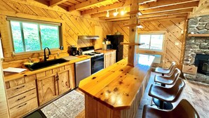 A rustic wooden kitchen with a central island, built-in appliances, and a stone fireplace.