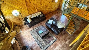A wooden interior with a black leather sofa, a coffee table, and a staircase.