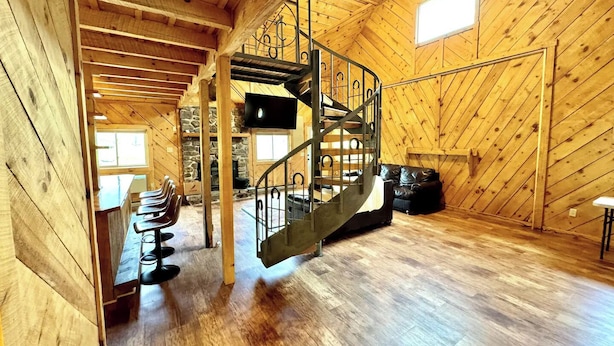 A spacious wooden cabin with a central staircase, a fireplace, and a television.