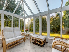 A conservatory with a glass ceiling, wicker furniture, and a view of a garden.