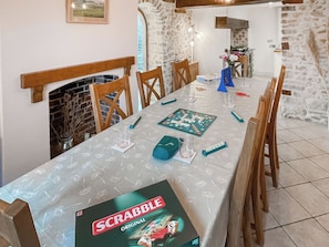 A dining area with a Scrabble game set on a table, wooden chairs, a fireplace, and stone walls.