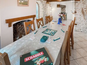 A dining area with a Scrabble game set on a table, wooden chairs, a fireplace, and stone walls. - Charming four-bed holiday home in Yarcombe sleeps eight. (Yarcombe)