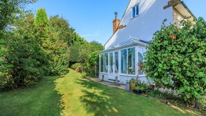 A house with a conservatory, surrounded by lush greenery and a well-maintained lawn. - Charming four-bed holiday home in Yarcombe sleeps eight. (Yarcombe)