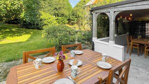 A wooden table set outdoors with chairs, a vase of flowers, and plates and cups. - Charming four-bed holiday home in Yarcombe sleeps eight. (Yarcombe)
