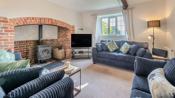 A living room with a brick fireplace, a flat-screen TV, a sofa set, and a lamp. - Charming four-bed holiday home in Yarcombe sleeps eight. (Yarcombe)
