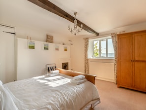 A bedroom with a bed, a wooden wardrobe, a fireplace, and a window with curtains. - Charming four-bed holiday home in Yarcombe sleeps eight. (Yarcombe)