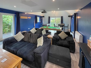 A modern living room with a pool table, dark sofas, and a dining area. - Charming four-bed holiday home in Yarcombe sleeps eight. (Yarcombe)