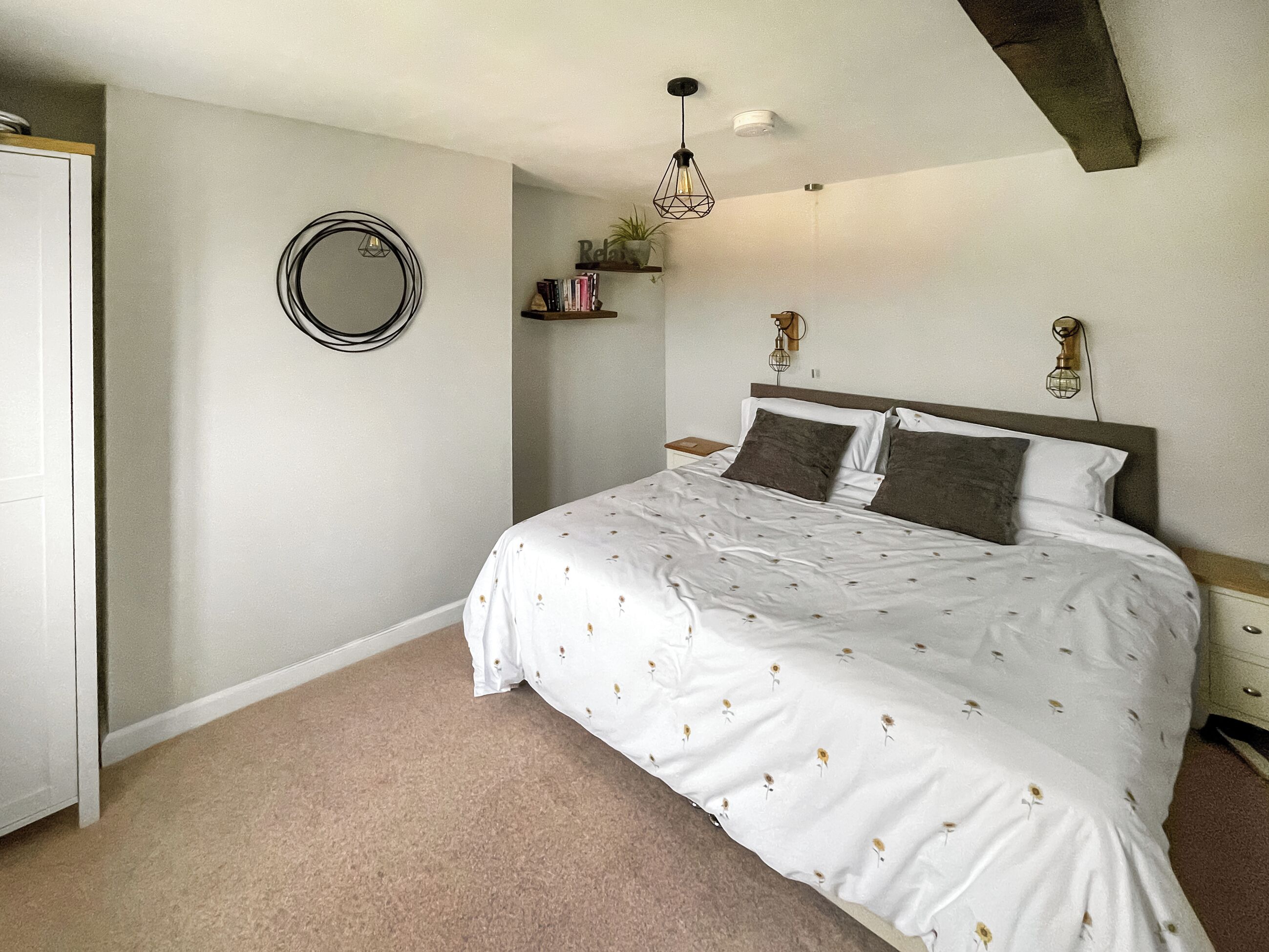 Une chambre à coucher avec un lit, un miroir rond, une petite étagère avec des livres et un luminaire suspendu.