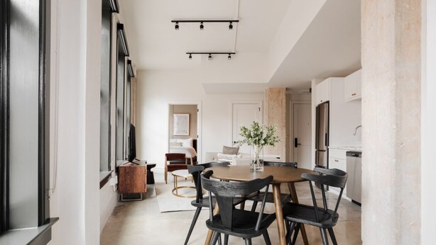 A modern kitchen with a central island, black chairs, and a wooden table.