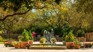 A garden with a fountain, potted plants, and a stone wall.