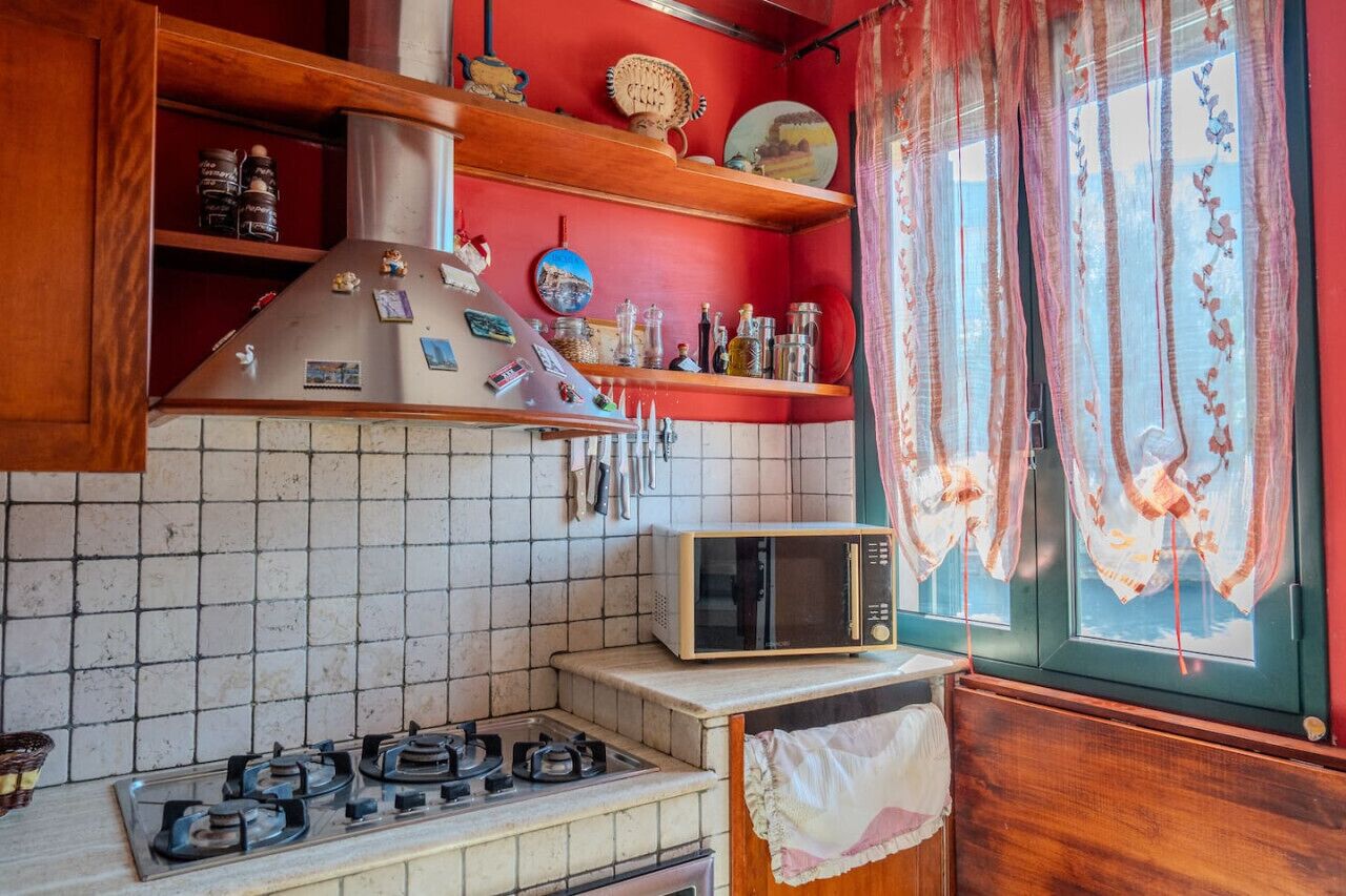 Una cocina con estufa a gas, microondas y pared roja con estanterías.