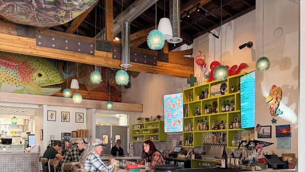 Un restaurant doté d’un bar, de poutres en bois au plafond, de luminaires sphériques suspendus et d’un tableau affichant le menu.