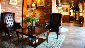 Un hall d’entrée accueillant avec un mur en briques, des fauteuils en cuir, une table basse en bois agrémentée d’une plante et un tapis à motifs.
