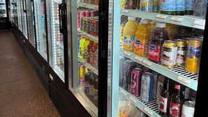 Une rangée de réfrigérateurs remplis de diverses boissons, notamment des sodas, des jus de fruits et de l’eau en bouteille.