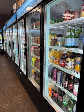 Una hilera de refrigeradores llenos de bebidas, como gaseosas, jugos y agua embotellada.