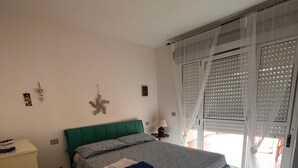 Un dormitorio con cama, mesita de noche, lámpara y ventana con persianas.