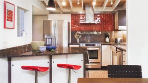 A modern kitchen with a granite countertop, stainless steel appliances, and red bar stools. - Cool Mid-Century Modern 3/2 (Austin)