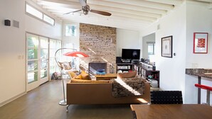 A spacious living room with a stone fireplace, a television, and a bookshelf. - Cool Mid-Century Modern 3/2 (Austin)