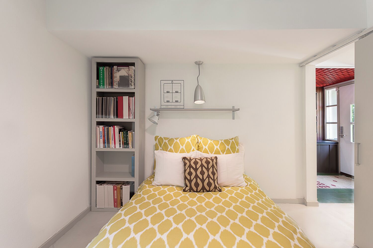 Un dormitorio con cama, una estantería y una lámpara colgante.