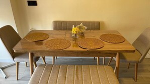 A dining table with four woven placemats, a glass vase with yellow flowers, and a bench in front.