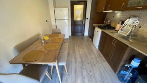 A compact kitchen with a dining table, chairs, a refrigerator, a dishwasher, and a tiled backsplash.