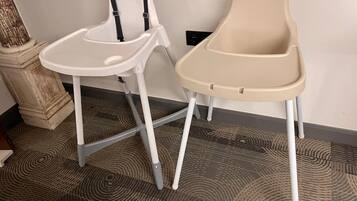 Dos sillas altas con bandejas, una blanca y otra color beige, sobre una alfombra estampada.
