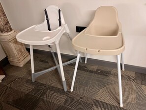 Twee kinderstoelen met tafelblad, één wit en één beige, staan op een kamerbreed tapijt.