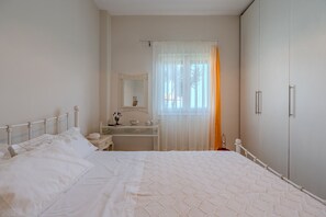A bedroom with a bed, a bedside table, a mirror, a wardrobe, and a window with sheer curtains. - Gallery House,near beach,pool, South Crete (Keratokambos)