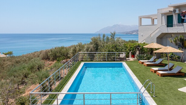 A rectangular swimming pool with a metal railing, surrounded by a well-maintained lawn and lounge chairs with umbrellas. - Gallery Villa with Pool, 300m Beach, Sea Views (Keratokambos)