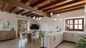 A modern kitchen with white cabinets, a wooden ceiling, and a dining area with a round table and chairs.