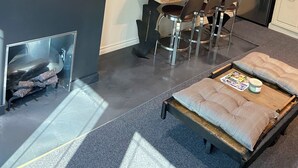 Un espacio habitable compacto con kitchenette, una zona de comedor con mesa y sillas de madera, un sofá con cojines estampados, un televisor montado en la pared y un refrigerador de acero inoxidable.