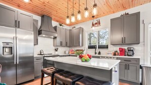 Een moderne keuken met roestvrijstalen apparatuur, een centraal eiland met barkrukken en een raam met uitzicht op bomen.