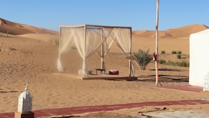 A desert scene with a tent-like structure featuring a canopy. - Luxury nomadic tented camp  (Merzouga)