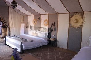 A tent-style bedroom with a bed, bedside table, lamp, and decorative wall elements. - Luxury nomadic tented camp  (Merzouga)