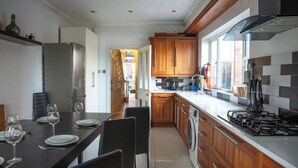 A modern kitchen with wooden cabinets, a gas stove, and a dining area with a table set for two. - Huge House in Derby City Centre | Free Parking (Derby)