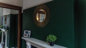A dark green wall with a gold-framed mirror and a small potted plant on a white mantelpiece. - Huge House in Derby City Centre | Free Parking (Derby)