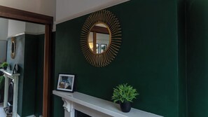 A dark green wall with a gold-framed mirror and a small potted plant on a white mantelpiece. - Huge House in Derby City Centre | Free Parking (Derby)