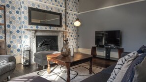 A living room with a fireplace, a television, and a patterned wallpaper.