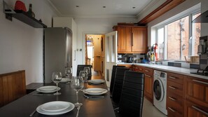 A modern kitchen with a dining area, wooden cabinets, a washing machine, and a view through the window.