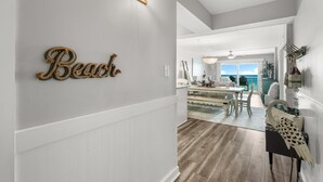 A hallway with a 'Beach' sign, a dining area with a chandelier, and a view of the outdoors. - NEW! Salt Life at PCB (Panama City Beach)