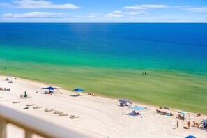 A beach with clear turquoise water, white sand, and several umbrellas and lounge chairs.