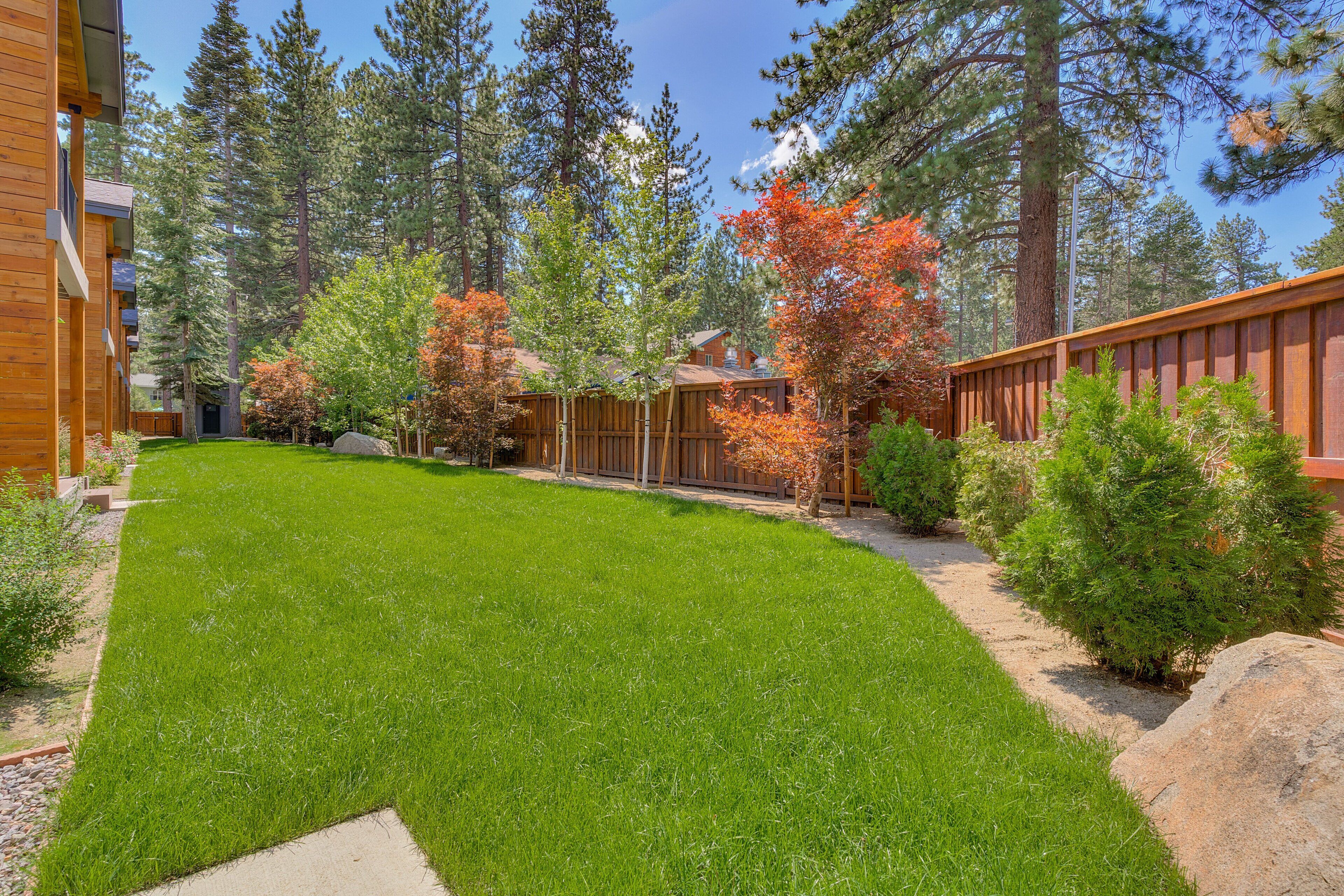 A well-maintained grassy yard with a wooden fence, surrounded by tall trees and a clear sky.