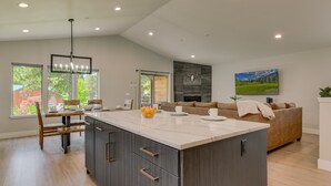 A modern kitchen with a large island, wooden dining table, and a cozy living area with a fireplace and a large window. - NEW! AC, Hot Tub, Grill, Newly Built, Open Floor Plan, Wifi, 6 of 6 – Emerald Bay Way (South Lake Tahoe)