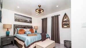 A bedroom with a bed, bedside tables, a nightstand, a bench, a ceiling fan, a wall-mounted shelf, and curtains. - Melrose 2 BR w/ large kitchen + fireplace + patio (Vista)