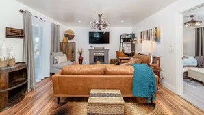 A modern living room with a brown leather sofa, a television, and a chandelier. - Melrose 2 BR w/ large kitchen + fireplace + patio (Vista)