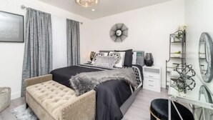 A modern bedroom with a large bed, a bedside table, a chair, a mirror, and a decorative wall piece.