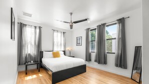 A modern bedroom with a large bed, a ceiling fan, and two windows with grey curtains. - East Austin Condo - 2 Bedrooms & Parking (Austin)