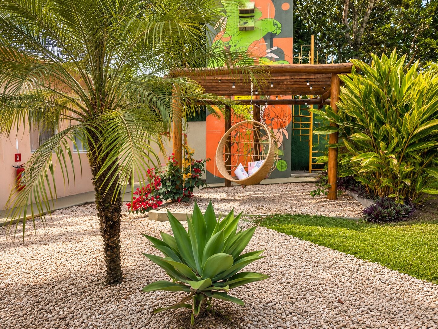 A garden with a hanging chair, palm trees, and a mural.