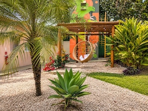Een tuin met een hangstoel, palmbomen en een muurschildering.